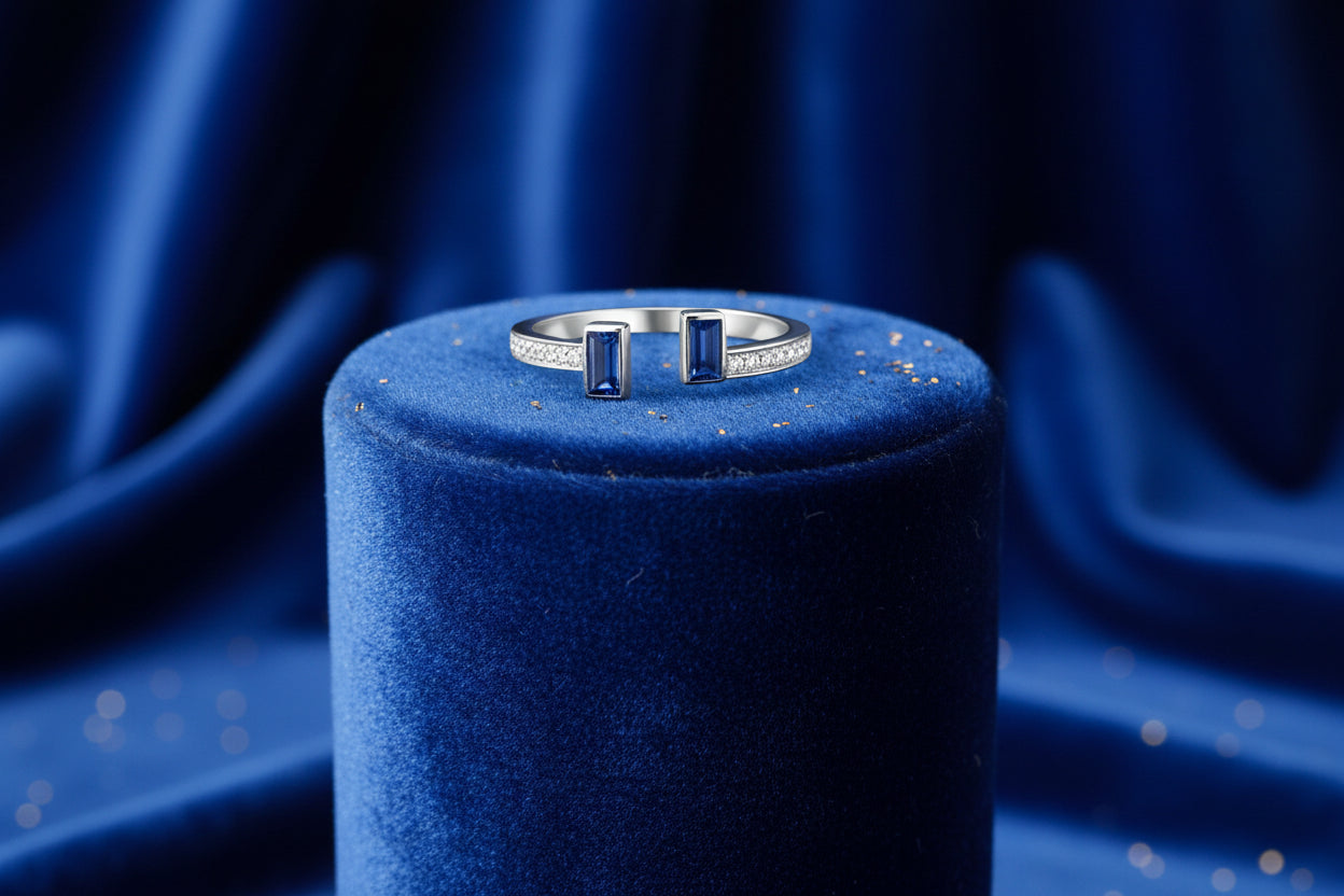 A white gold band ring with a blue sapphire and diamond embellishment, displayed on a warm background with candles.